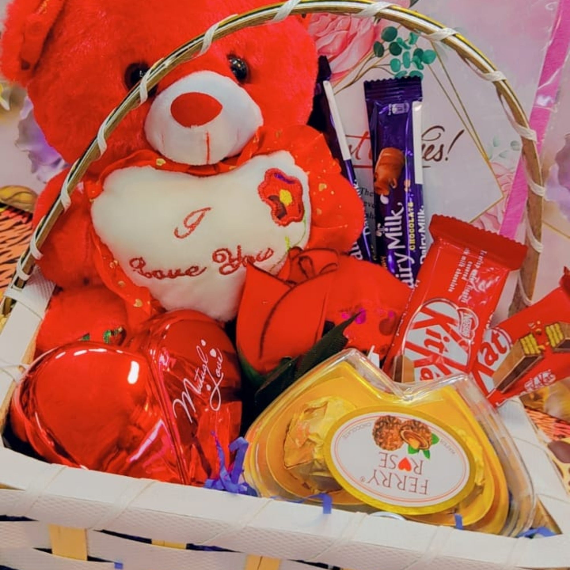 Gift basket with a red teddy bear, chocolates, and a heart-shaped box of candy.