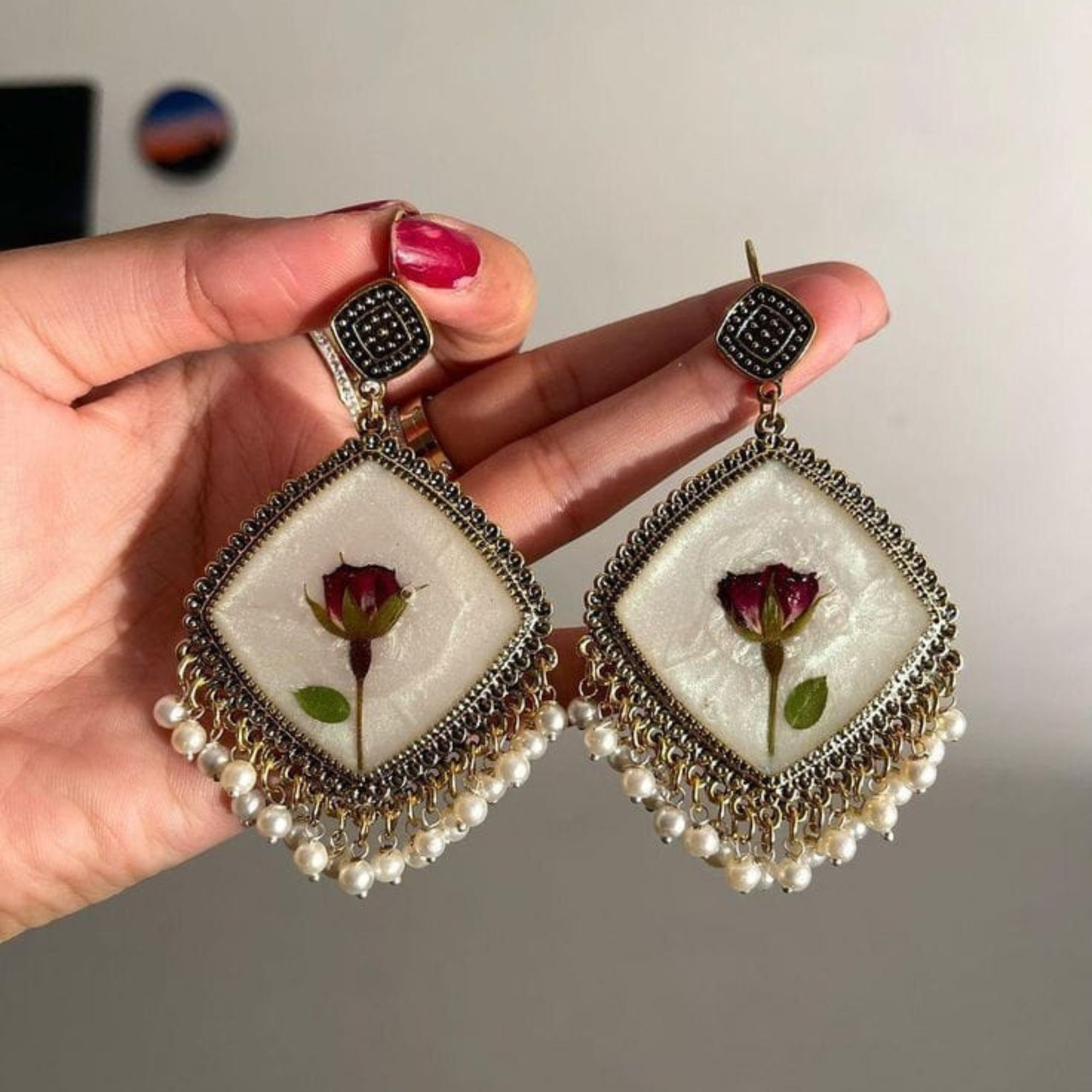 Earrings with rose design held by a hand against a neutral background
